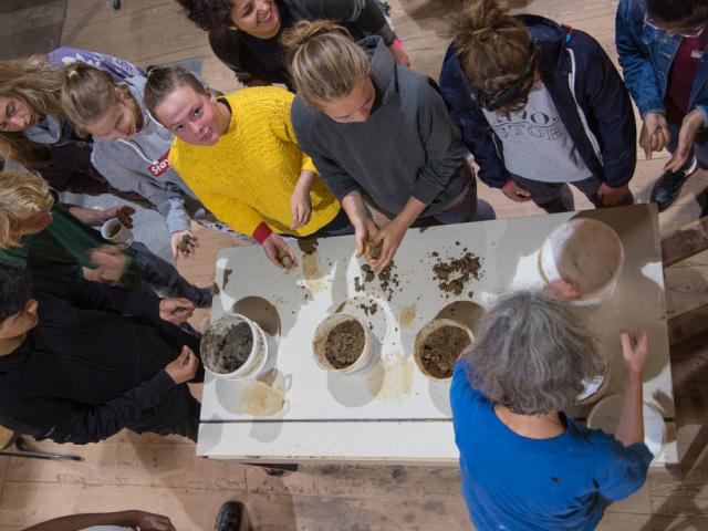 Anrühren von Lehmputzmörtel. | Foto: Hendrik Silbermann (ARTWORKs) Anrühren von Lehmputzmörtel in der Werkstatt. Die Teilnehmenden stehen neben Maßbechern mit Lehmputzen. | Foto: Hendrik Silbermann (ARTWORKs)