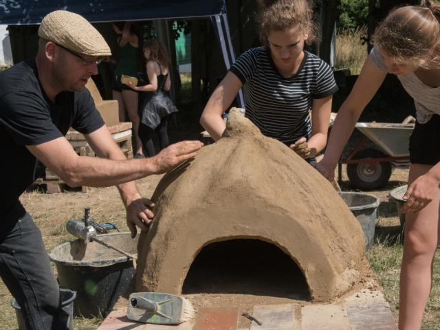 Der "Kürbisofen" in den letzten Zügen. Sechshändig wird mit Lehm verputzt. |Foto: Hendrik Silbermann (ARTWORKs) Rundofen verputzen. |Foto: Hendrik Silbermann (ARTWORKs)