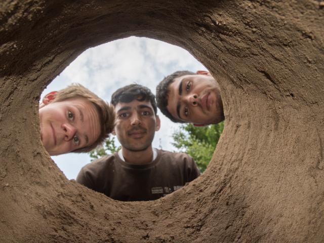Blick in den Lehmbackofen. | Foto: Hendrik Silbermann (ARTWORKs) Blick in den Lehmbackofen durch drei Teilnehmende. | Foto: Hendrik Silbermann (ARTWORKs)
