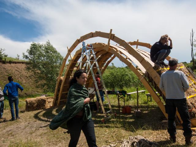 Die Teilnehmenden richten die Strohballen auf die Unterkonstruktion. | Foto: Hendrik Silbermann (ARTWORKs) Aufnahme der Brücke beim Aufbau.