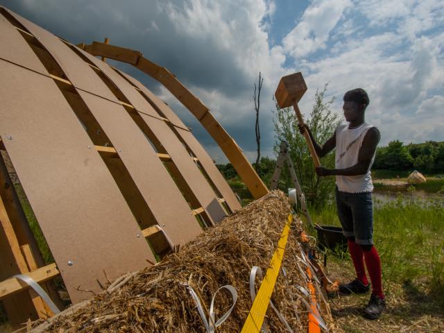 Mit einem großen Hammer werden die Strohballen auf der Brücke befestigt. | Foto: Hendrik Silbermann (ARTWORKs) Die Strohballen werden auf der Brückenkonstruktion mit einem großen Hammer befestigt.