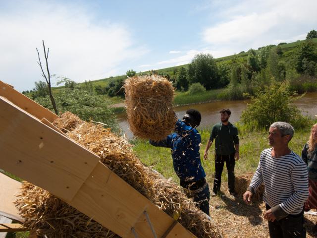 Nach und nach kommen die Strohballen auf die Brücke. | Foto: Hendrik Silbermann (ARTWORKs) Die Strohballen werden von einem Teilnehmenden nach oben auf die Brücke getragen.