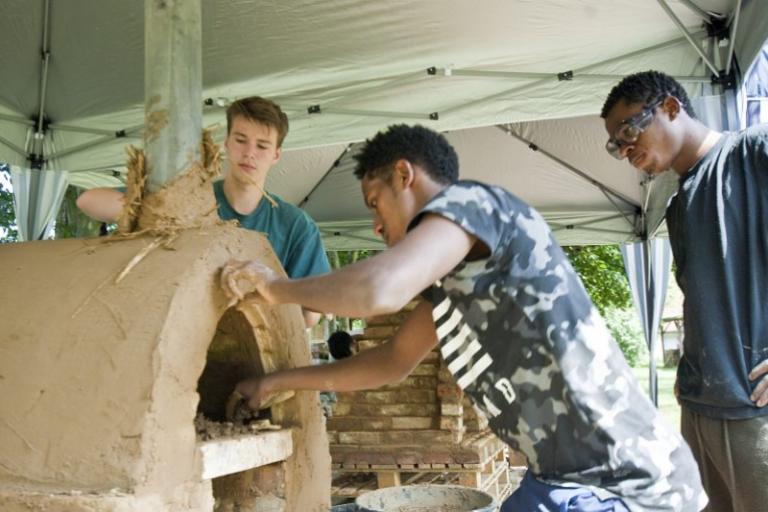 Jugendliche stehen um einen Ofen aus Lehm und bauen diesen fertig. | Foto: Hendrik Silbermann (ARTWORKs)